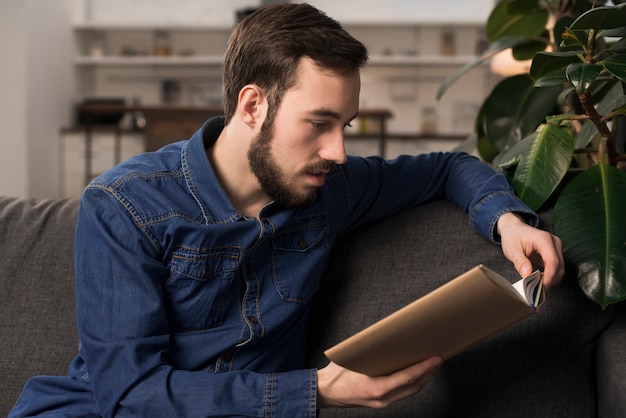 Mann, der auf Couch und Lesebuch sitzt