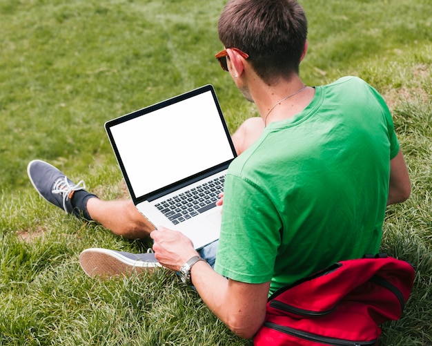 Mann, der auf dem Gras hält Laptop sitzt