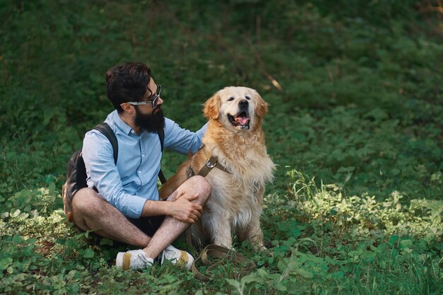 Mann, der auf dem Gras ruht, das gekreuzte Beine mit seinem Hund sitzt