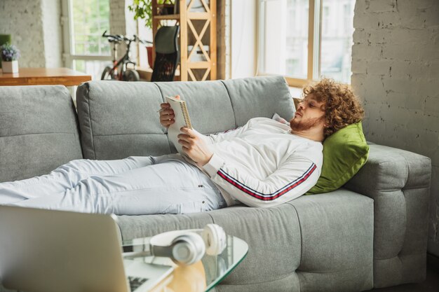 Mann, der auf der Couch liegt und eine Zeitschrift liest