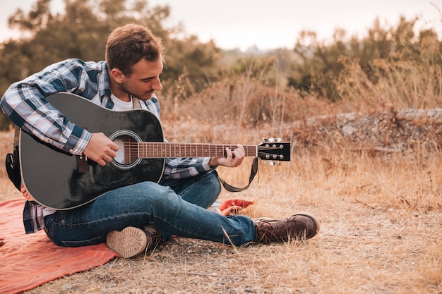 Mann, der auf der Decke spielt Gitarre sitzt