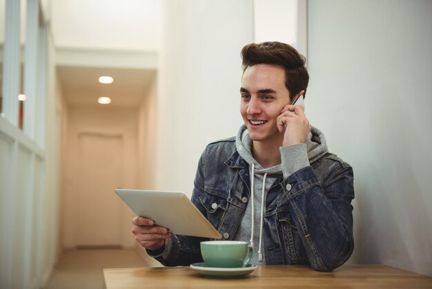 Mann, der auf Handy spricht, während digitales Tablett hält