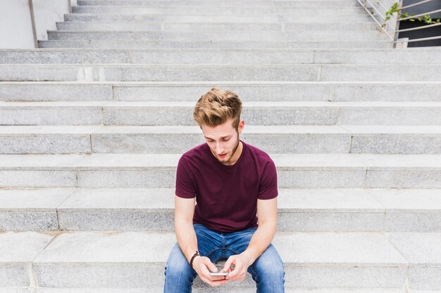 Mann, der auf Treppenhaus unter Verwendung des Mobiltelefons sitzt