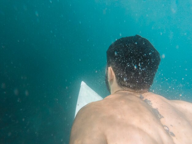 Mann, der auf weißem Surfbrett Unterwasser schwimmt