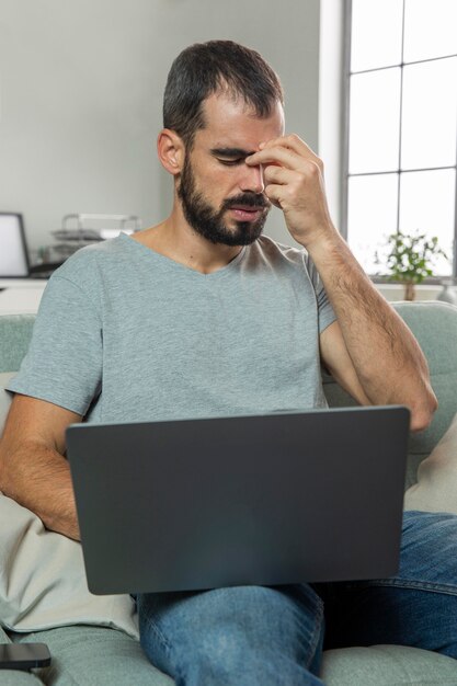 Mann, der Augenschmerzen beim Arbeiten am Laptop von zu Hause fühlt