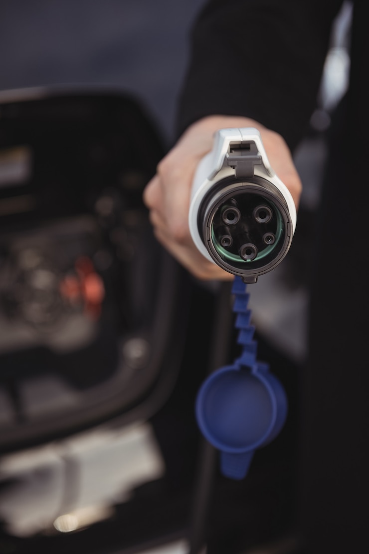 Kostenlose Foto mann, der autoladegerät an der elektrofahrzeugladestation hält