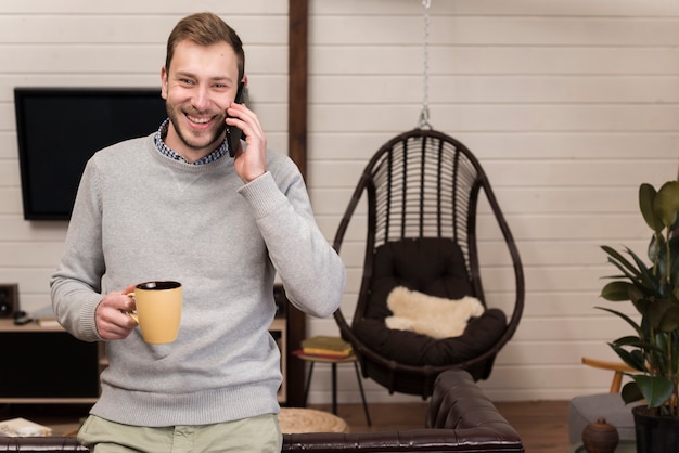 Mann, der Becher hält und zu Hause am Telefon spricht