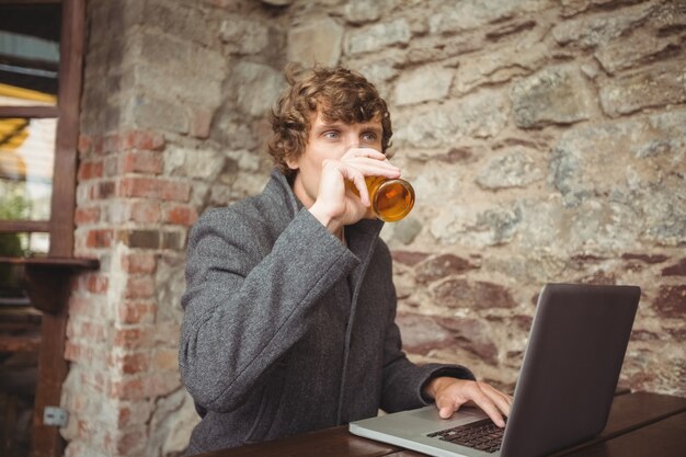 Mann, der Bier beim Verwenden des Laptops hat