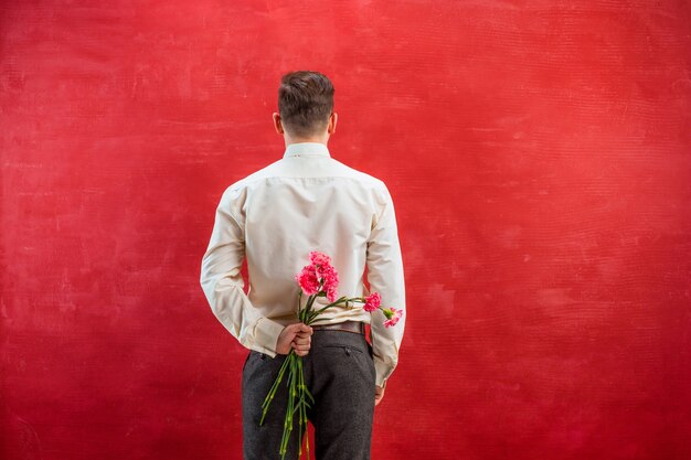 Mann, der Blumenstrauß der Nelken hinter zurück auf rotem Studio hält