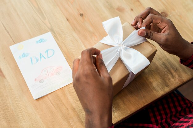 Mann, der Bogen auf Geschenkbox nahe Grußkarte löst