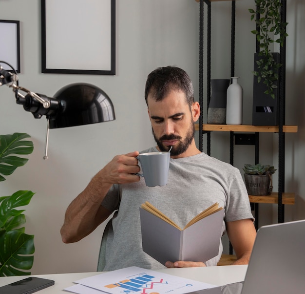 Mann, der buch liest und kaffee trinkt, während er von zu hause aus arbeitet