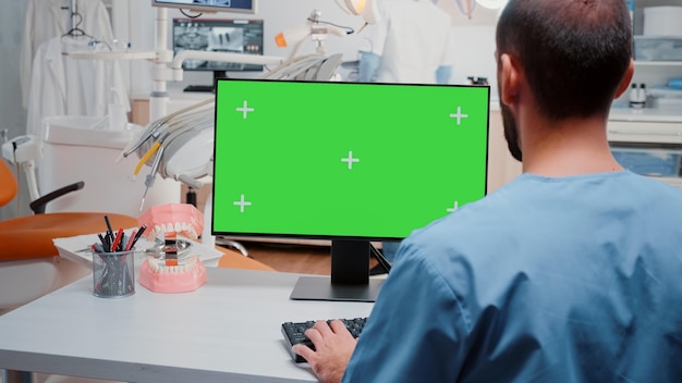 Mann, der Computer mit horizontalem grünem Bildschirm für Zahnmedizin im Kabinett betrachtet. Assistent, der mit Chroma-Key und isoliertem Hintergrund auf dem Monitor für stomatologische Pflege und Untersuchung arbeitet