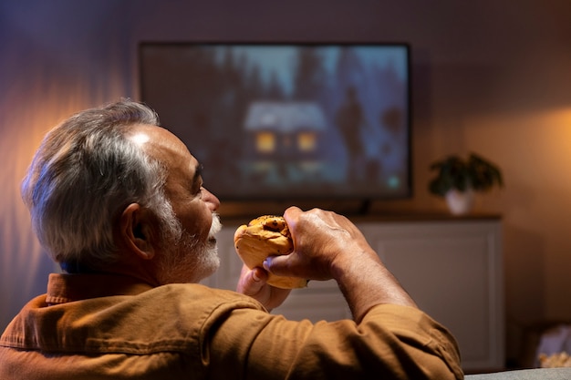 Mann, der das Essen genießt, während er allein zu Hause ist und fernsieht