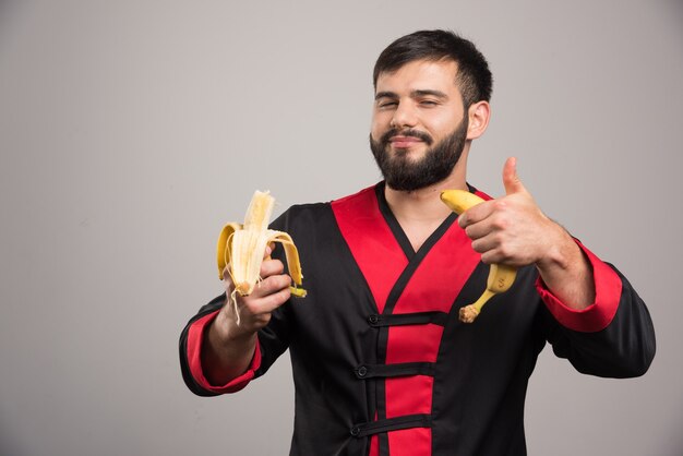 Mann, der Daumen oben zeigt und eine Banane auf grauer Oberfläche isst.