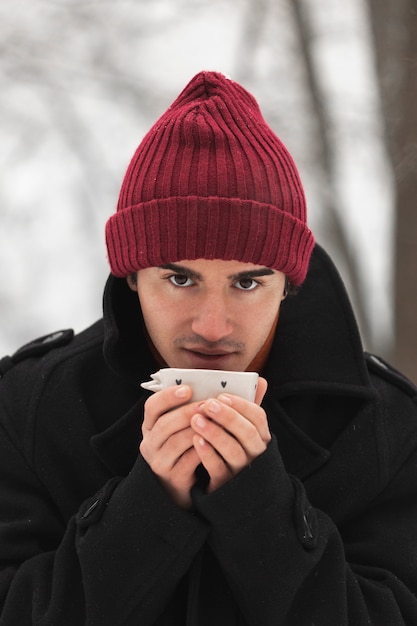 Mann, der den roten Hut nippt von einer Tasse Tee trägt