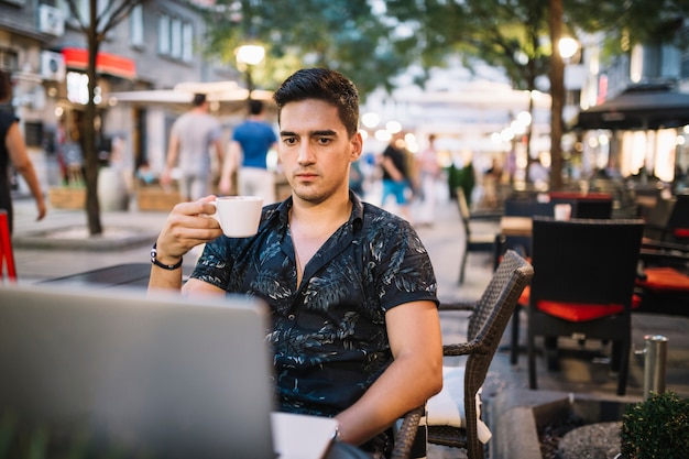 Mann, der den Tasse Kaffee betrachtet Laptopschirm hält