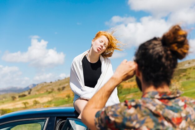 Mann, der die Gesicht verziehende Frau sitzt auf Autodach fotografiert
