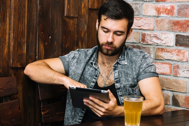 Mann, der digitale Tablette mit Bier auf Tabelle verwendet