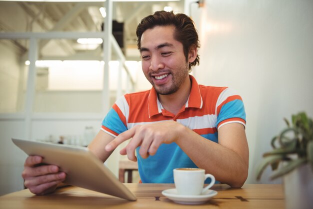 Mann, der digitale Tablette mit Kaffeetasse auf Tisch verwendet