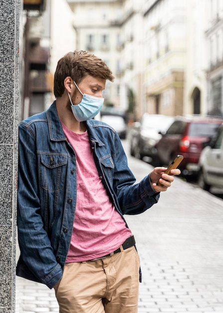 Mann, der durch sein Telefon schaut, während er eine medizinische Maske draußen trägt