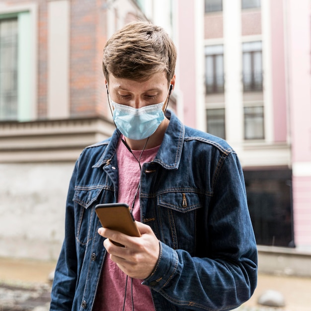Mann, der durch sein Telefon schaut, während er eine medizinische Maske trägt