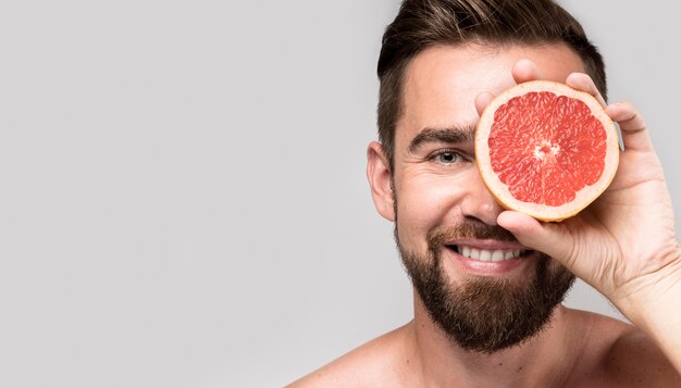 Mann, der ein Auge mit einer halbierten Grapefruit bedeckt