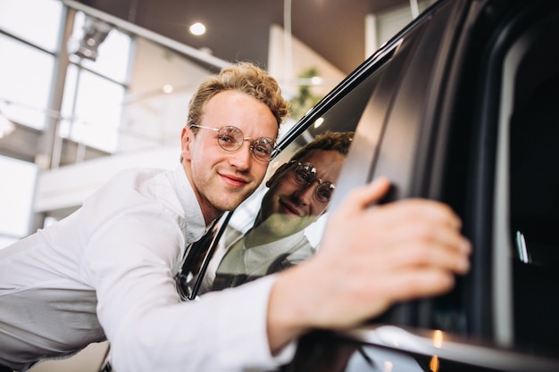 Mann, der ein Auto in einem Autosalon umarmt