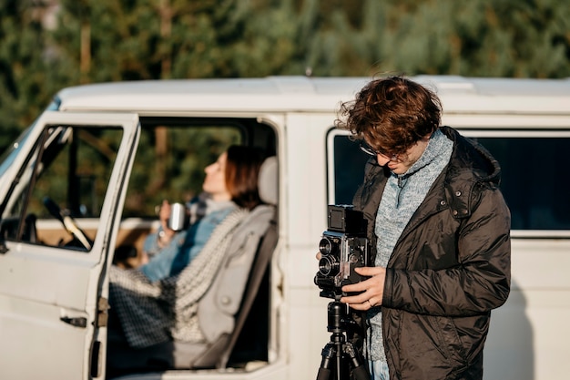Kostenloses Foto mann, der ein foto mit einer retro-kamera neben seinem van macht