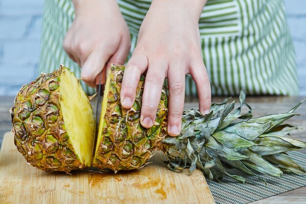 Mann, der eine frische Ananas auf einem hölzernen Schneidebrett schneidet