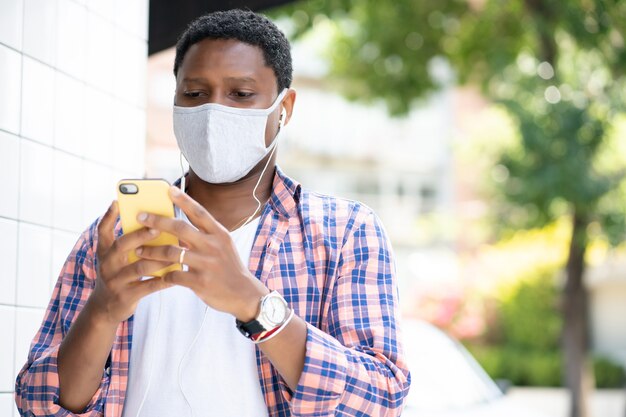 Mann, der eine Gesichtsmaske trägt und sein Mobiltelefon benutzt, während er im Freien steht