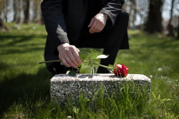 Kostenloses Foto mann, der eine rose zu einem grabstein auf dem friedhof bringt