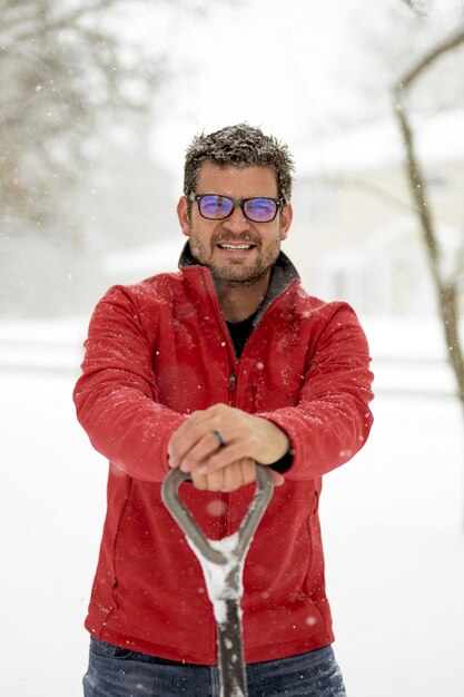 Mann, der eine rote Winterjacke mit seinen Händen auf einer Schneeschaufel trägt