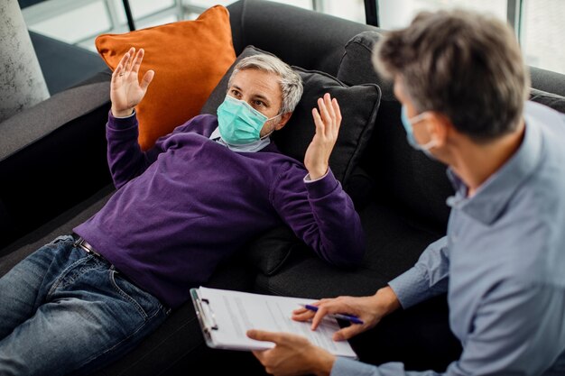 Mann, der eine schützende Gesichtsmaske trägt, während er mit einem Psychiater über seine Probleme spricht