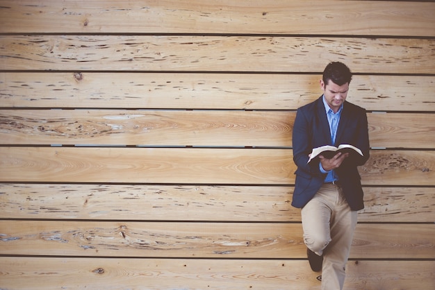 Kostenloses Foto mann, der einen anzug trägt, der sich an die wand lehnt, während er die bibel liest