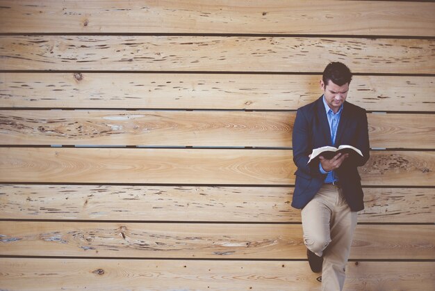 Mann, der einen Anzug trägt, der sich an die Wand lehnt, während er die Bibel liest