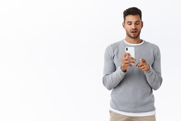 Mann, der einen Freund leitet, wie er auf seinem Smartphone fotografiert Attraktiver bärtiger Mann in grauem Pullover mit Handy-Look-Bildschirm und Kamera, um schöne Aufnahmen zu machen