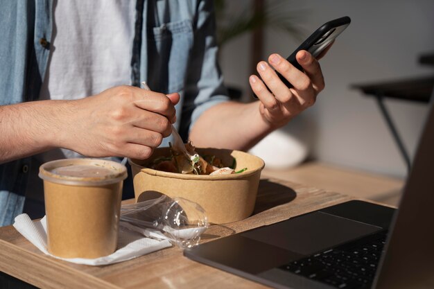 Mann, der Essen zum Mitnehmen genießt und Smartphone verwendet