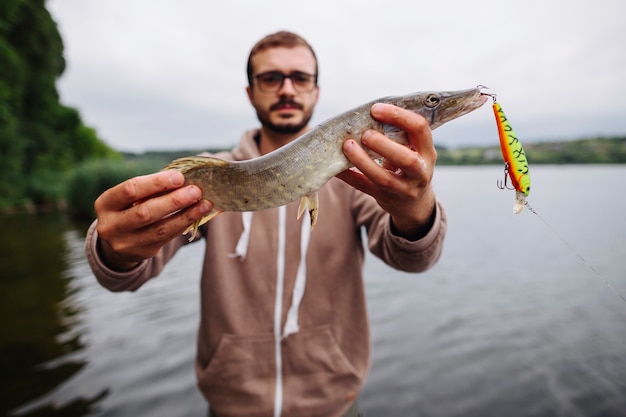 Kostenloses Foto mann, der frisch gefangenen fisch mit köderhaken zeigt