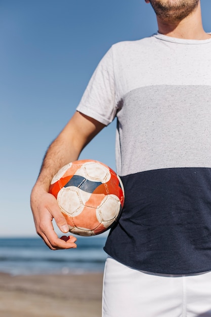 Kostenloses Foto mann, der fußball am strand hält