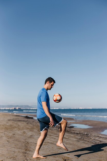 Mann, der Fußball am Strand spielt