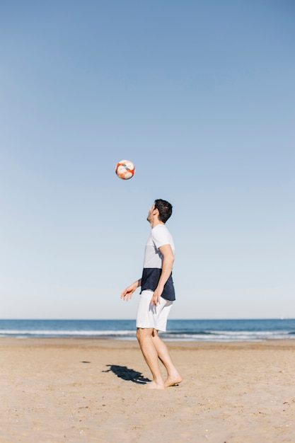 Mann, der Fußball am Strand spielt