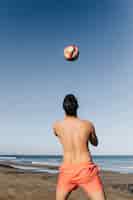 Kostenloses Foto mann, der fußball am strand spielt