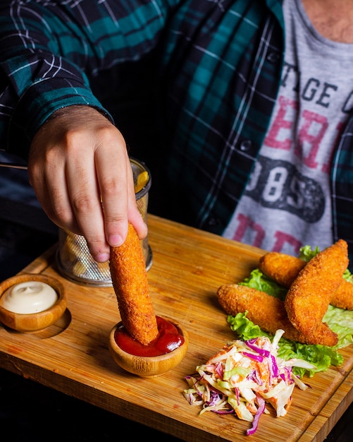 Mann, der gebratene Hühnerfinger in Ketchup eintaucht