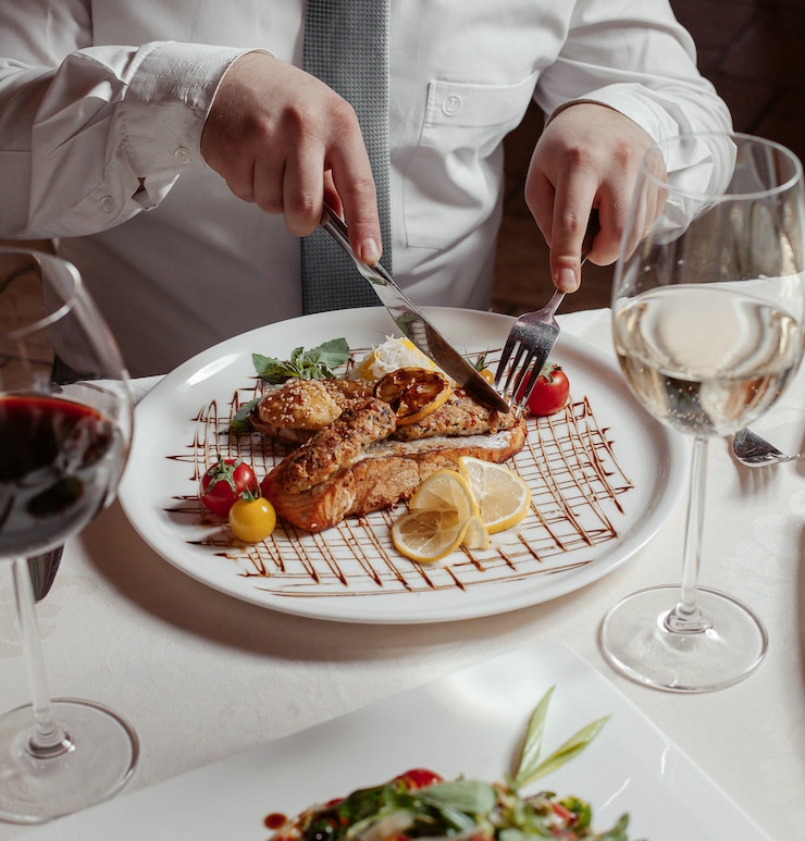 Kostenlose Foto mann, der gegrillten lachs mit reis, lula kebab, läusen, tomaten, wein schneidet