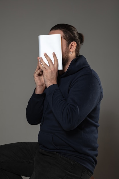 Mann, der Gesicht mit Buch bedeckt, während auf grauer Wand liest