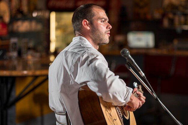 Mann, der Gitarre spielt und auf Mikrofon in einer Bar singt