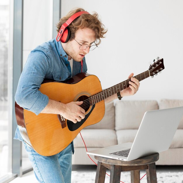 Mann, der Gitarre spielt und Laptop betrachtet