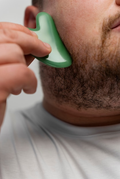 Mann, der gua sha auf seinem gesicht für hautpflege verwendet