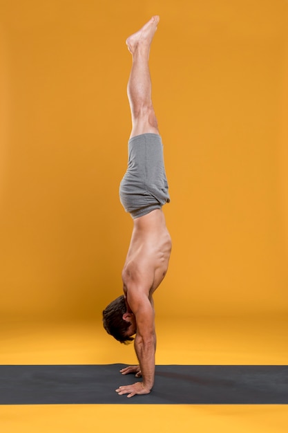 Kostenloses Foto mann, der handstandhaltung auf yogamatte tut