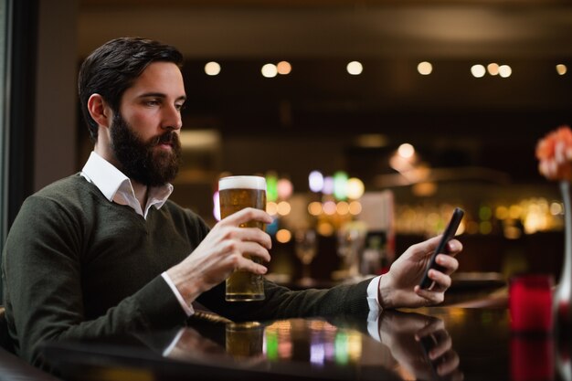 Mann, der Handy beim Glas Bier betrachtet